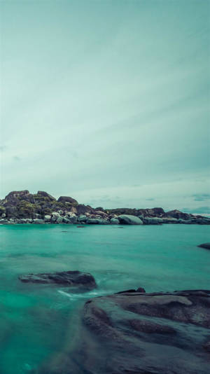 在多雲的天空下，藍綠色的海水繞過深色岩石流動。