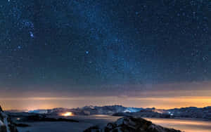積雪的山峰下，星空燦爛的夜空，山谷燈光閃爍。