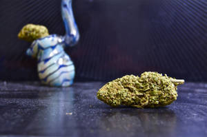 一個綠色大麻花蕾和一個藍色玻璃水煙槍在深色表面上。