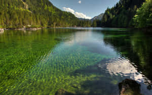 一個寧靜的山間湖泊，在藍天下有翠綠色的湖水和森林覆蓋的山丘。