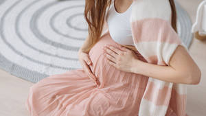 孕婦在家中的螺旋形地毯上坐著，輕輕抱著肚子。 — 孕婦 壁紙