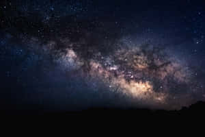 銀河系在佈滿星星的夜空下，在山巒輪廓上方發光。