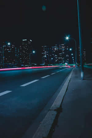 夜間城市高速公路，帶有紅色汽車燈光條紋和明亮的建築物。 — 暮光 壁紙