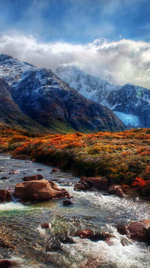 山間溪流流經秋色景觀，背景有雪覆蓋的山峰。