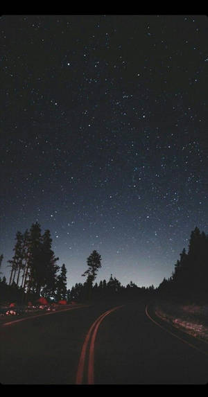 夜晚一條黑暗蜿蜒的道路，星空下，兩旁有樹木。 — 日落大道 壁紙