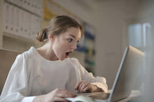 身穿白色襯衫的女子在辦公室對著筆記本電腦屏幕倒吸一口氣