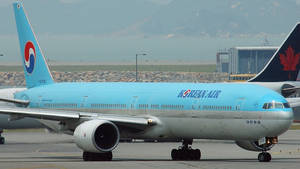 大韓航空波音777飛機停在機場停機坪，背景有山脈