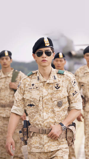 年輕士兵穿著軍裝戴著太陽眼鏡，在戶外站著，身後有部隊。
