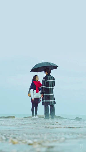 一對情侶在雨中的海灘上撐傘牽手。