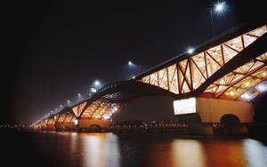 一座照明鋼橋在夜間跨越河流，帶有發光的倒影。 — 韓國 壁紙