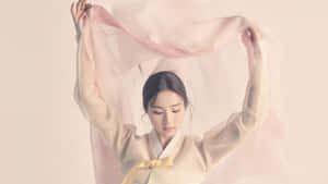 穿著傳統韓服的女子，面帶寧靜表情，手持一條飄逸的粉紅色絲巾。