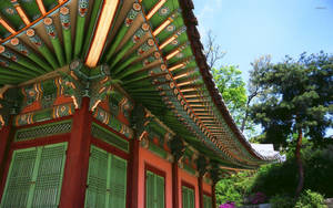 色彩繽紛的傳統韓國寺廟屋頂，帶有華麗圖案和綠色百葉窗，周圍環繞著樹木。 — 日產 Skyline GTR R33 壁紙