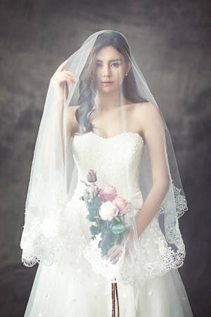 一位身穿白色蕾絲婚紗的新娘手持粉紅玫瑰。