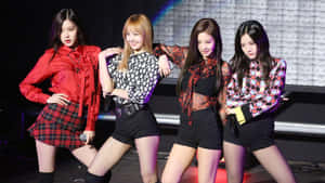 四位女K-pop表演者在燈光明亮的舞台上自信擺姿勢，穿著色彩繽紛的服裝。