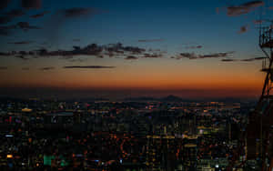 黃昏時分的城市天際線，燈光閃爍，天空橙色