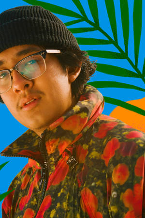 戴冷帽和眼鏡的年輕男子，穿著帶棕櫚葉和藍色背景的花卉外套。