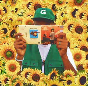 戴綠色帽同背心嘅人，喺向日葵前面攞住兩張音樂唱片。 — Tyler the creator GIF 壁紙