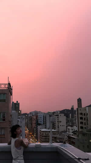 人在屋頂上凝視著城市天際線上的粉紅色日落。 — 夏日氣息 壁紙