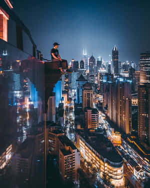 一個人坐在玻璃陽台上，俯瞰夜晚閃爍的城市。 — 天空景觀 壁紙