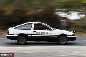 白色AE86跑車在道路上疾馳，背景模糊。