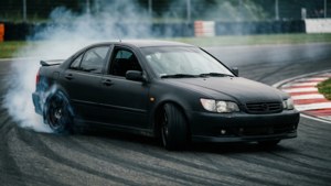 黑色汽車在賽道漂移，輪胎冒煙
