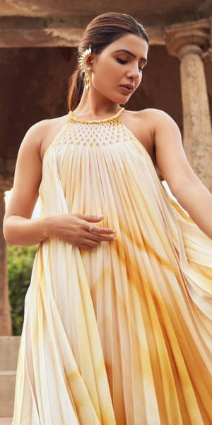 身穿飄逸金黃色長裙的女性站在古老石柱下。