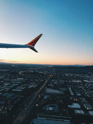 日落時分城市上空的飛機機翼，閃爍的街道和山脈