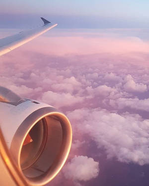 飛機機翼和引擎在日落時飛越粉紅色和紫色的雲層。 — 天空景觀 壁紙