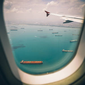 從飛機窗戶俯瞰海洋，有貨船和遠方的城市。 — 天空景觀 壁紙