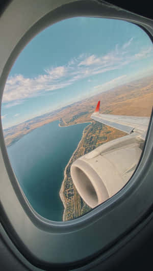 從乘客窗戶看到的飛機機翼和引擎，位於海岸水域和陸地之上。