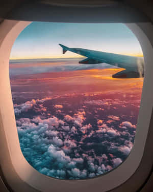 在色彩繽紛的日落中，從飛機窗戶俯瞰雲層上的飛機翼。 — 天空景觀 壁紙