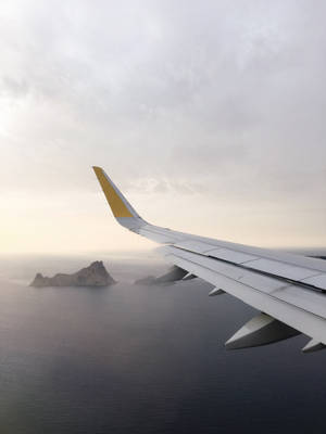 飛機機翼在海洋上空飛行，下方有岩石島嶼，天空多雲。