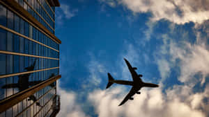飛機在藍天白雲下飛過玻璃建築。 — 天空景觀 壁紙