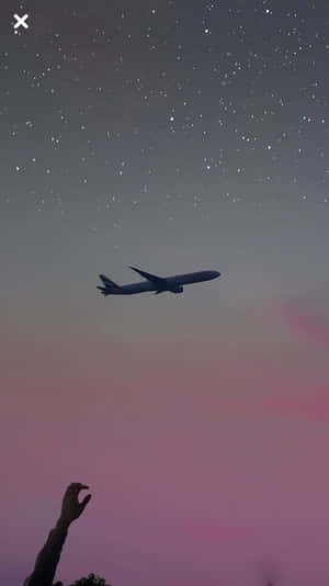 一隻手伸向在星夜粉紅和紫色天空下飛行的飛機。
