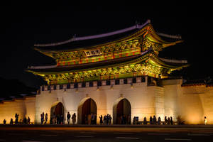 夜間被照亮的傳統韓國大門，人們聚集在周圍。