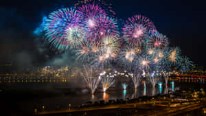 五彩繽紛的煙火在夜間水面上倒映的城市天際線上綻放。