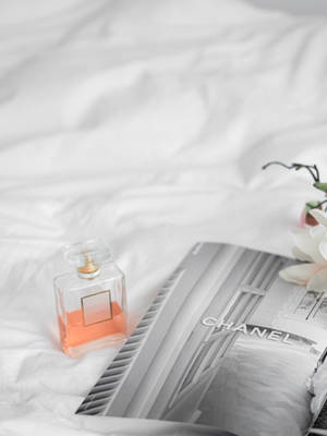 一個香水瓶和 Chanel 雜誌放在白色床上，伴有一朵蘭花。