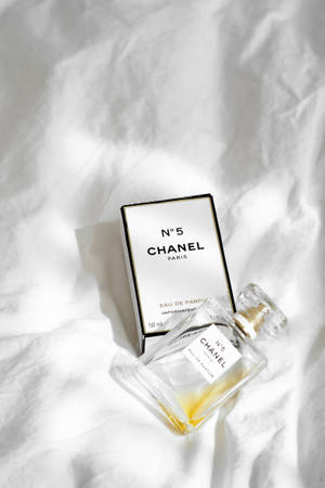 Chanel No 5 香水瓶和盒子放在白色布上，帶有柔和陰影。