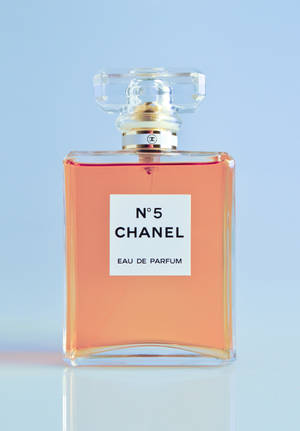 Chanel No 5 香水瓶，裝有桃色液體，置於反光表面上。