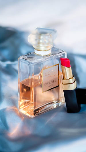 Chanel 香水瓶和紅色唇膏在藍色緞布上。