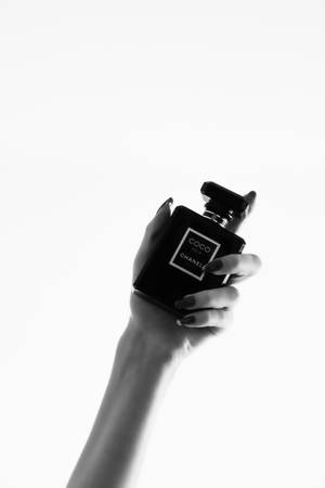 一隻手在白色背景下握著一個黑色的 Chanel 香水瓶。