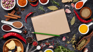 空白食譜筆記本被色彩繽紛的香料和廚房工具包圍，置於深色表面上。