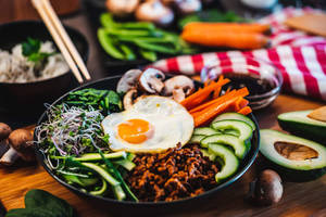 一碗色彩繽紛的韓國石鍋拌飯，配以雞蛋和蔬菜，置於木桌上。 — 清新 GIF 壁紙