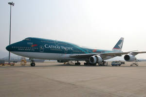 國泰航空波音747在機場停機坪上，有地勤人員和設備。