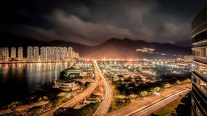 繁華城市的夜景，靠近水和山脈，有發光的建築和高速公路。