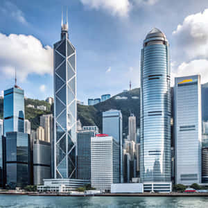 現代玻璃摩天大樓在藍天下從水面升起，背景是翠綠的山丘。