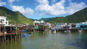 在一個被綠山環繞的寧靜沿海村莊中，充滿活力的高腳屋和船隻。 — 香港 壁紙