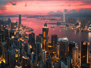 日落時分的香港城市景觀，燈火通明的摩天大樓和港灣水域。