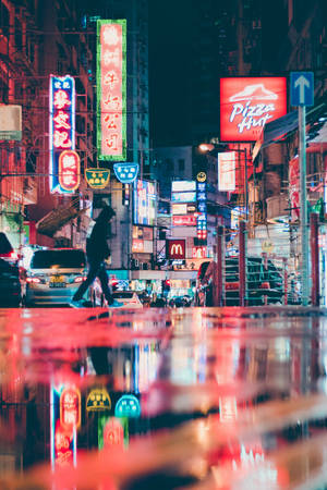行人穿過霓虹燈照亮的濕漉漉的夜晚街道，倒影閃爍