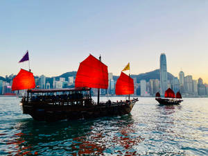 紅帆帆船在日落時分駛過香港現代化的天際線。